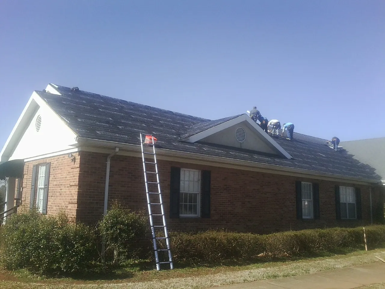 Crew tearing shingles off a brick ranch roof with a ladder set — Emergency Roof Repair work by our crew in Gwynedd Valley