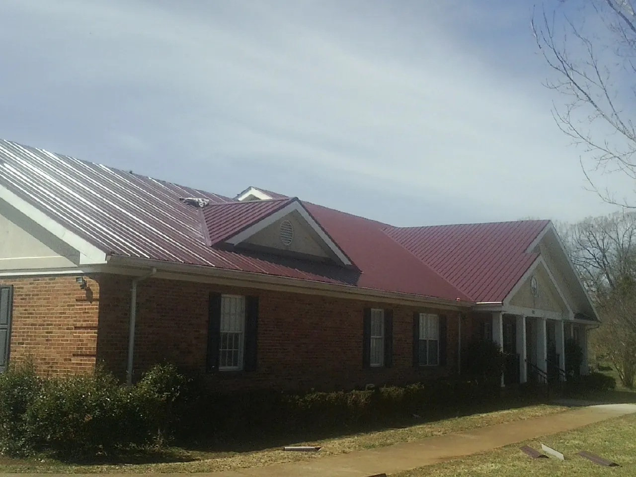 Red metal roof with gabled entries on a long brick building, from a Hail Damage Roof Repair job in Gwynedd Valley