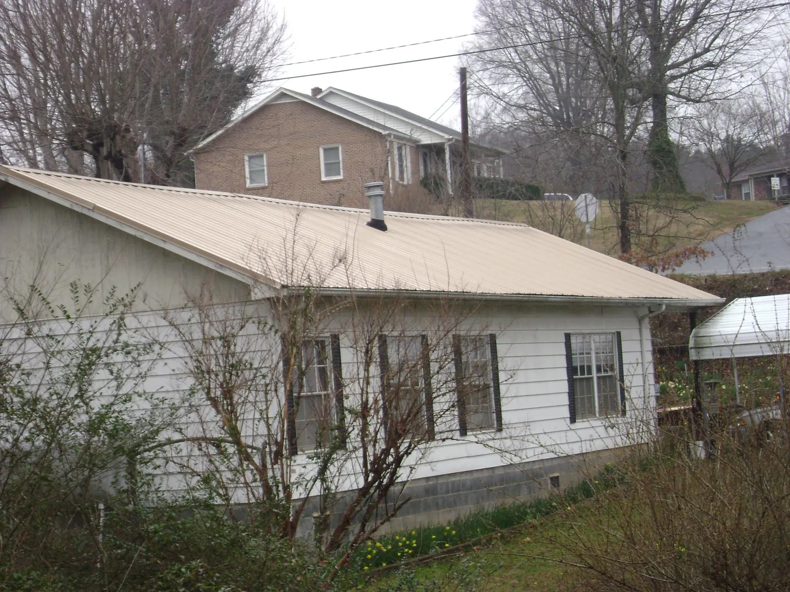 Tan metal roof on a white sided house set into a hillside — Commercial Roofing by Roofing Brothers in Gwynedd Valley